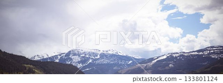 Flat illustration is showing snow-capped mountains above coniferous valley with cumulus clouds 133801124