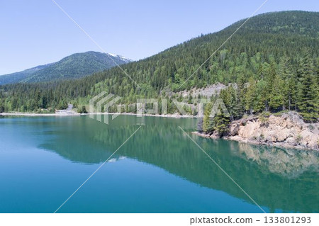 Forest on mountain by blue river against sky Forest on mountain by blue river against sky 133801293