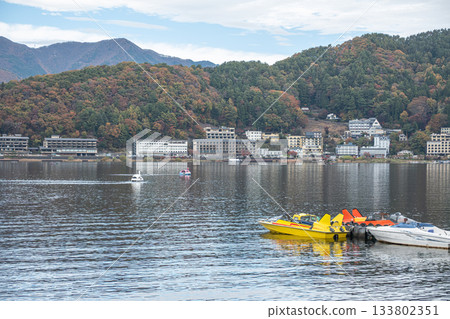 Lake Kawaguchi, Fujikawaguchiko, Minamitsuru District, Yamanashi, Japan, Yellow pedal boats docked on lake with mountains and town in background 133802351