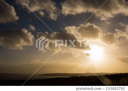 Golden sun is shining through scattered cumulus clouds over calm bay with headland in flat design Golden sun is shining through scattered cumulus clouds over calm bay with headland in flat design 133802792