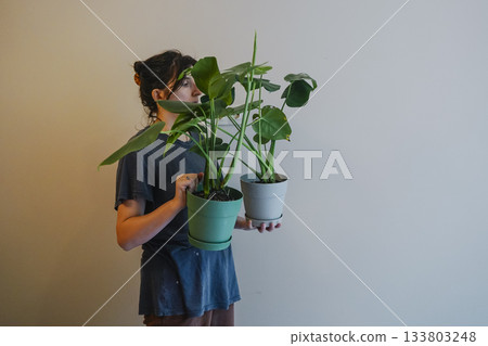 Young Woman Holding Two Potted Monstera Plants Indoors Young Woman Holding Two Potted Monstera Plants Indoors 133803248