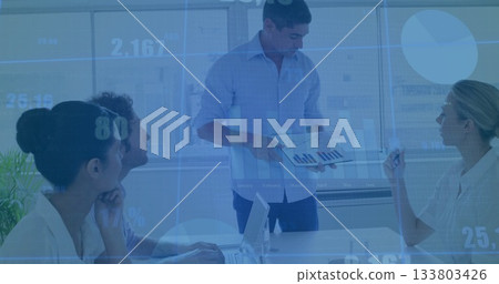 Presenting man in button-down shirt displaying bar chart on tablet at conference table, with laptop 133803426