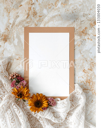 Blank White Card Mockup with Kraft Paper Border, Decorated with Orange Gerbera Flowers and Lace on Marble Background, Wedding Invitation Concept. 133804030