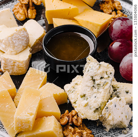 Tasty cheese platter with grapes, walnuts, and honey in a cozy setting Tasty cheese platter with grapes, walnuts, and honey in a cozy setting 133804066