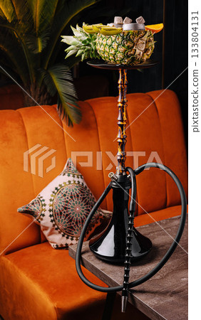 Unique pineapple hookah placed on a stylish table in a cozy lounge Unique pineapple hookah placed on a stylish table in a cozy lounge 133804131