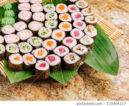 Delicious sushi rolls arranged on a bamboo plate with green garnish Delicious sushi rolls arranged on a bamboo plate with green garnish 133804157