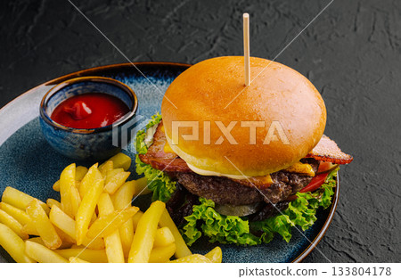 Juicy burger with bacon and fries served on a blue plate Juicy burger with bacon and fries served on a blue plate 133804178