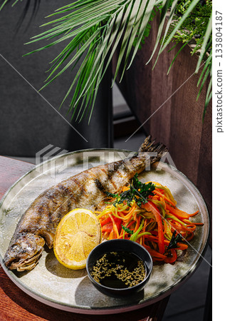 Grilled fish served with fresh vegetables and lemon on a wooden table 133804187