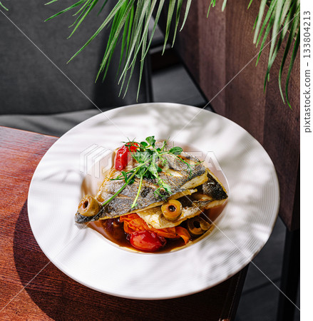 Delicious grilled fish served on a plate with vegetables and sauce 133804213