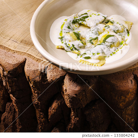 Fresh ravioli served with cream sauce and herbs on a rustic wooden table Fresh ravioli served with cream sauce and herbs on a rustic wooden table 133804242