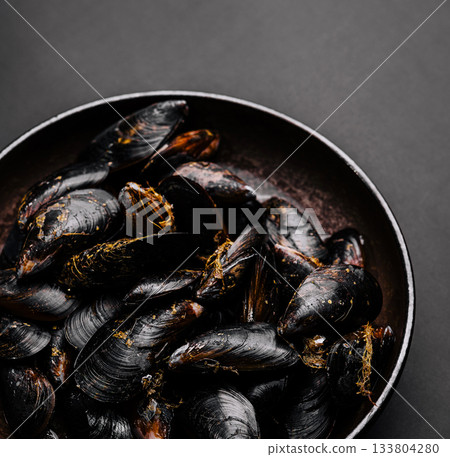 Freshly cooked mussels served in a dark bowl on a simple background 133804280