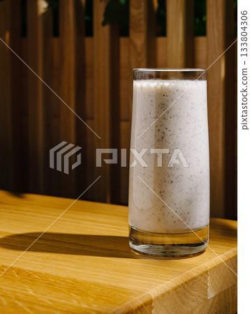Creamy smoothie glass on wooden table in bright sunlight Creamy smoothie glass on wooden table in bright sunlight 133804306