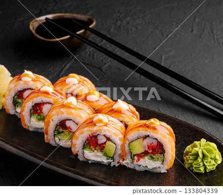 Colorful sushi rolls arranged neatly on a dark plate with wasabi and sauce Colorful sushi rolls arranged neatly on a dark plate with wasabi and sauce 133804339