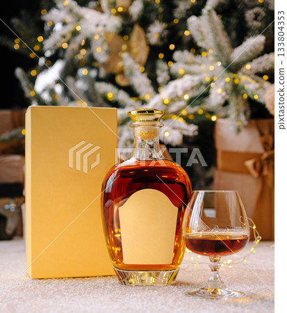 Festive whiskey bottle and glass by a Christmas tree with gifts 133804353
