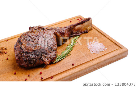 Deliciously cooked ribeye steak on a wooden cutting board with herbs 133804375
