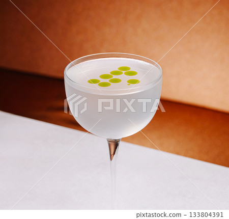 Cocktail served in a stylish glass with green dots on top 133804391