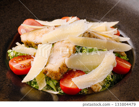 Grilled fish salad with cherry tomatoes and cheese on a dark plate 133804479