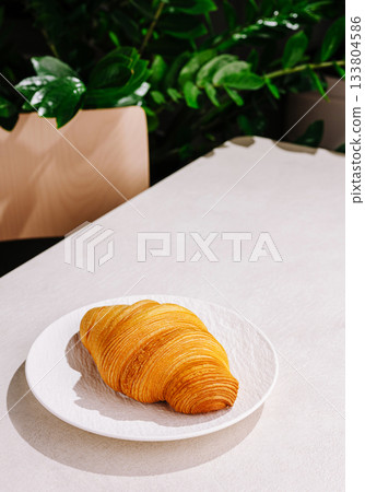 Freshly baked croissant on a plate in a cozy setting with greenery Freshly baked croissant on a plate in a cozy setting with greenery 133804586