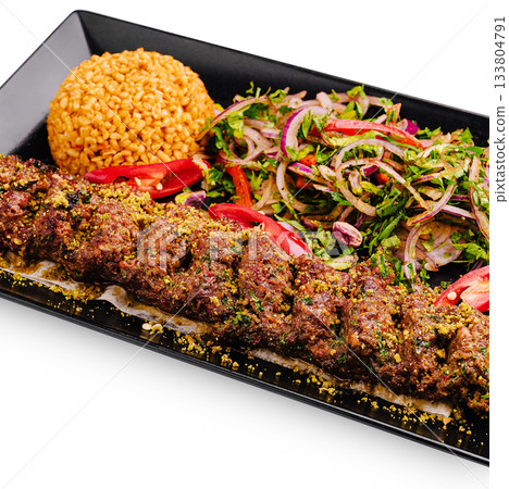 Spiced kebab with bulgur and fresh salad on a black plate Spiced kebab with bulgur and fresh salad on a black plate 133804791