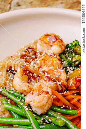 Delicious shrimp stir-fry served on a round plate with noodles and vegetables Delicious shrimp stir-fry served on a round plate with noodles and vegetables 133804835