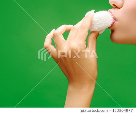 Woman enjoying a sweet treat with a green background in a bright setting Woman enjoying a sweet treat with a green background in a bright setting 133804977