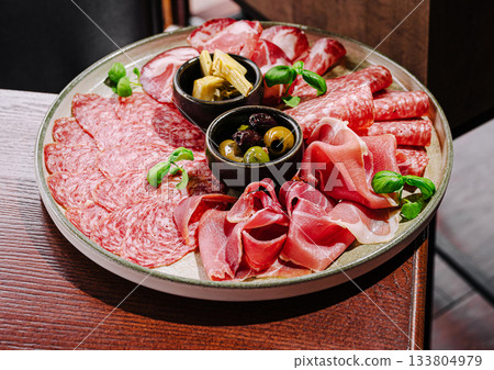 Savory charcuterie platter with meats and olives served on a wooden table 133804979