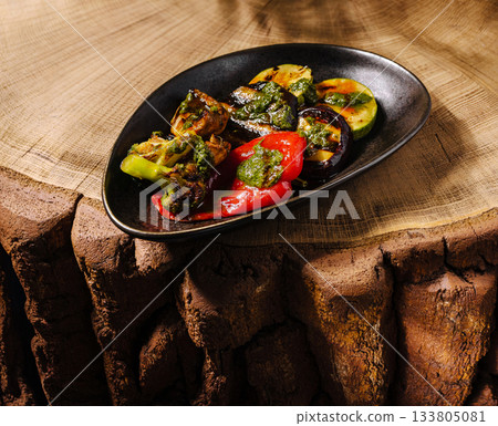 Grilled vegetables served on a sleek black plate with wooden background 133805081