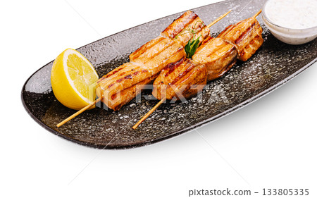 Delicious grilled salmon skewers with lemon and sauce on a black plate Delicious grilled salmon skewers with lemon and sauce on a black plate 133805335
