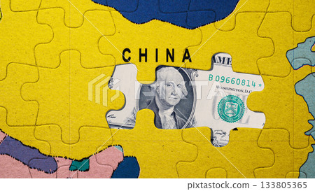 Jigsaw puzzle of a world map with the country of China in yellow. A missing puzzle piece reveals an American dollar bill. Economic relationship and interdependence between China and the United States 133805365