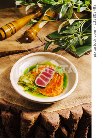 Freshly prepared tuna dish on wooden table with green garnish and orange puree 133805498
