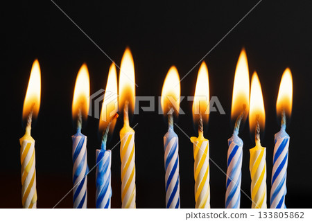 Yellow and blue birthday candles burning with soft warm flames on black background with copy space. Festive candles composition symbolizing celebration, joy, and bright holiday mood. Yellow and blue birthday candles burning with soft warm flames on black background with copy space. Festive candles composition symbolizing celebration, joy, and bright holiday mood. 133805862