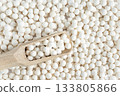 White dry tapioca pearls in wooden scoop on tapioca background. Top view of raw tapioca starch balls used for bubble tea or desserts. Tapioca pearls as healthy gluten free ingredient. 133805866