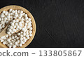 Organic tapioca pearls in wooden bamboo bowl on black table top view with copy space. Spoon scooping white dry tapioca pearls, cooking ingredient, gluten free food, healthy eating. 133805867