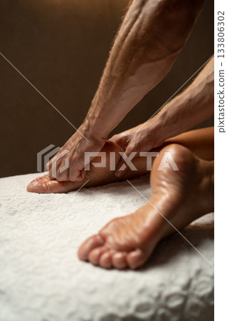 Close-up of a professional therapist performing a relaxing foot and leg massage in a spa, with oil on the skin, promoting wellness, relaxation, and circulation in a calm atmosphere. 133806302