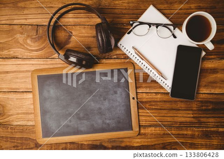 Blank chalkboard-style tablet is resting on wooden desk, showing headphones, smartphone, coffee Blank chalkboard-style tablet is resting on wooden desk, showing headphones, smartphone, coffee 133806428