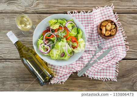Fresh salad in bowl by wine bottle on wooden table 133806473