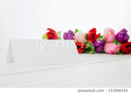 Flat design is showing blank white folded tent card on white tabletop with blurred colorful tulips 133806542