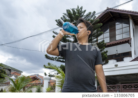 Indonesian southeast asian man is drinking water from a bottle while taking a break during exercise outdoors. Sport activity Indonesian southeast asian man is drinking water from a bottle while taking a break during exercise outdoors. Sport activity 133806705