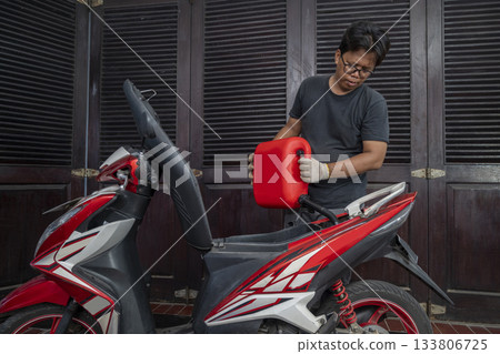 Indonesian southeast asian repairman refilling the gasoline fuel into the tank after repairing a motorcycle in a workshop Indonesian southeast asian repairman refilling the gasoline fuel into the tank after repairing a motorcycle in a workshop 133806725