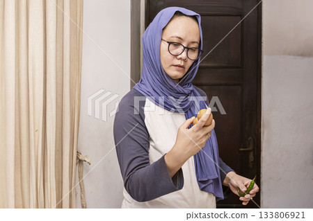 Woman wearing a blue scarf is holding a knife and cutting a piece of fruit 133806921
