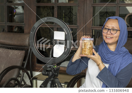 Indonesian hijab woman is holding a jar of food and doing livestream for selling at home 133806948