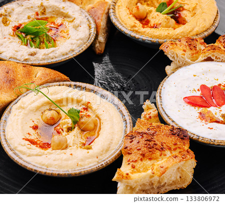 Delicious selection of hummus served with fresh bread on a black platter 133806972