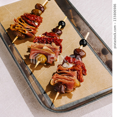Savory skewers featuring sun-dried tomatoes, olives, and cured meats 133806986
