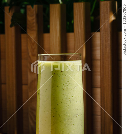 Refreshing green smoothie served in tall glass against wooden backdrop Refreshing green smoothie served in tall glass against wooden backdrop 133807009