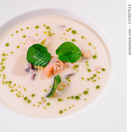 Soup with salmon, greens, and herbs presented elegantly in a white bowl 133807013