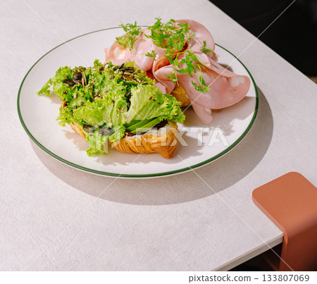 Delicious croissant with fresh lettuce and sliced ham served on a plate 133807069