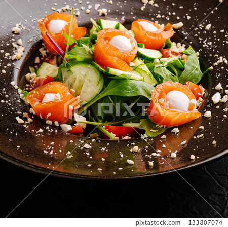 Fresh salmon salad with greens and vegetables on a dark plate 133807074