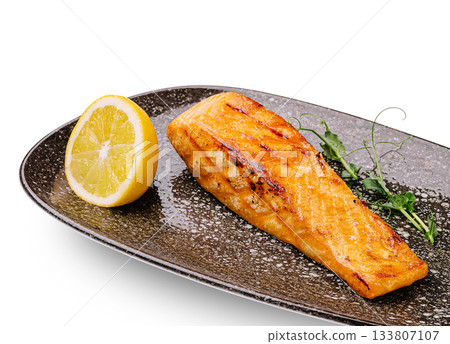 Grilled salmon fillet served with lemon and fresh greens on a black plate Grilled salmon fillet served with lemon and fresh greens on a black plate 133807107