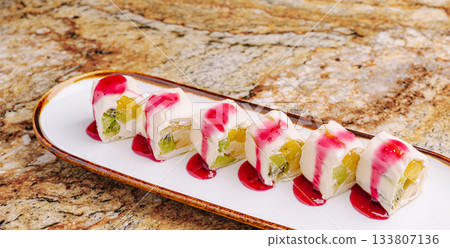 Elegant sushi rolls with fruit and vibrant sauce on a marble table 133807136