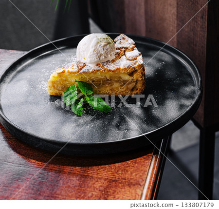 Delicious apple cake served with ice cream on a dark plate Delicious apple cake served with ice cream on a dark plate 133807179